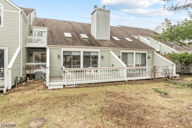 back of house featuring a shingled roof, a chimney, a yard, and a balcony