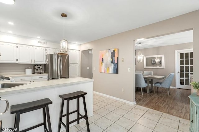 kitchen featuring white cabinets, light countertops, hanging light fixtures, freestanding refrigerator, and a kitchen bar