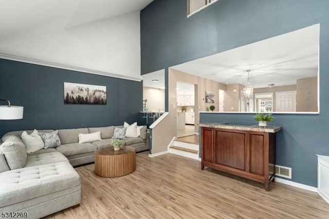 living area with a chandelier, light wood finished floors, visible vents, and baseboards