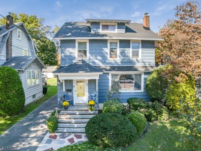 american foursquare style home with a shingled roof, driveway, and a chimney