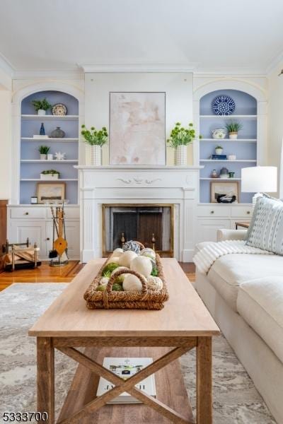 living room with built in shelves, ornamental molding, a fireplace, and wood finished floors