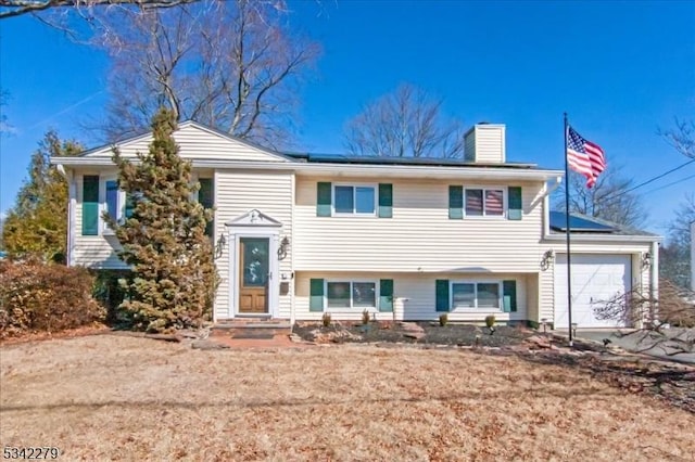 bi-level home featuring a chimney, an attached garage, and solar panels