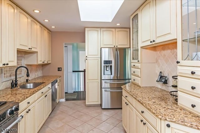 kitchen with appliances with stainless steel finishes, a skylight, cream cabinetry, and a sink