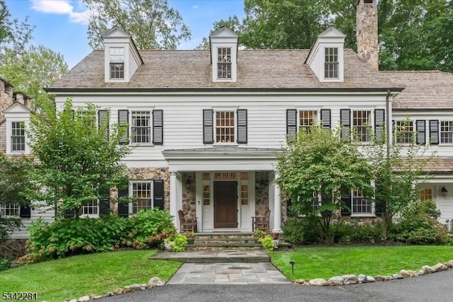 view of front of house featuring stone siding, a chimney, and a front lawn