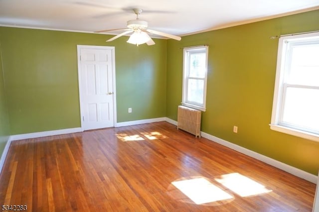 unfurnished room with baseboards, radiator, wood finished floors, and a ceiling fan