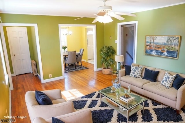 living area with light wood-style floors, baseboards, radiator, and ceiling fan