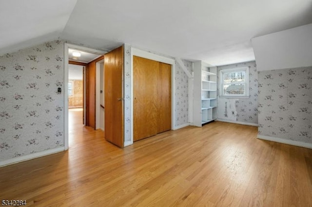 interior space with baseboards, wallpapered walls, light wood-style floors, and vaulted ceiling