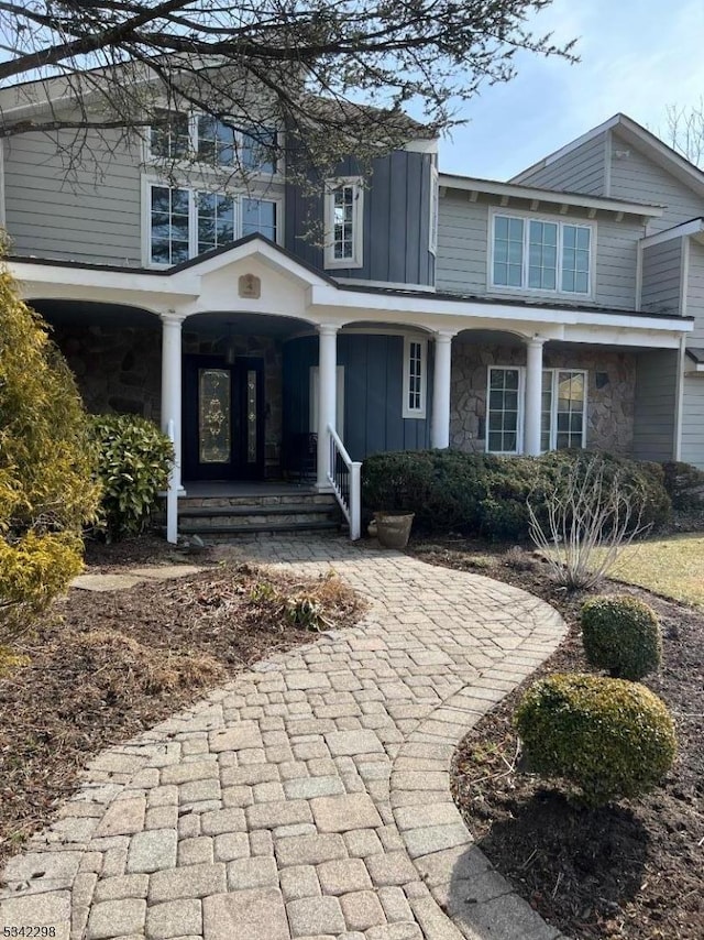 view of front facade with board and batten siding, stone siding, and covered porch