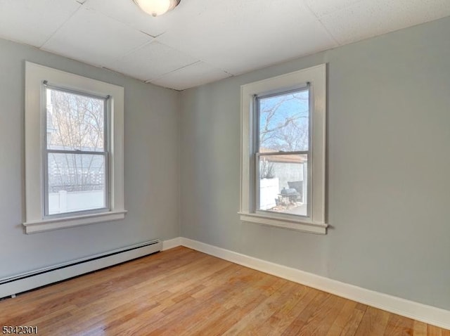 spare room featuring a drop ceiling, baseboards, baseboard heating, and light wood finished floors