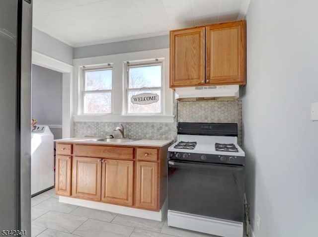 kitchen with backsplash, under cabinet range hood, light countertops, gas stove, and a sink