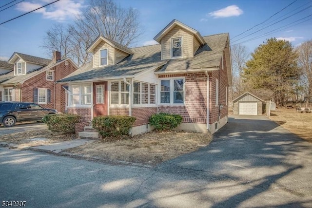 new england style home featuring brick siding, an outdoor structure, a detached garage, and aphalt driveway