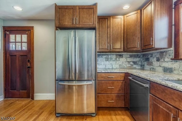 kitchen with light wood-style floors, appliances with stainless steel finishes, decorative backsplash, and light stone counters