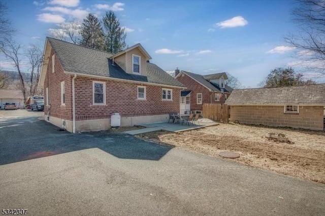 exterior space featuring a shingled roof, an outbuilding, brick siding, and a patio