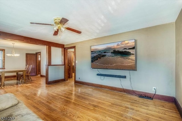 living area featuring ceiling fan with notable chandelier, baseboards, and wood finished floors