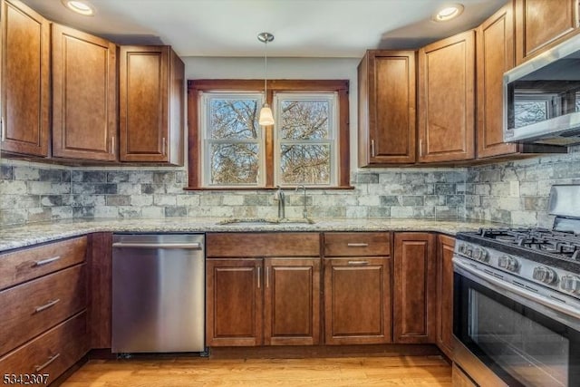 kitchen with decorative backsplash, light stone countertops, stainless steel appliances, light wood-type flooring, and a sink