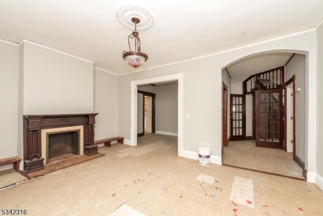 unfurnished living room featuring arched walkways, ornamental molding, a fireplace with flush hearth, and baseboards