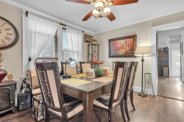 dining space with a wood stove, a ceiling fan, ornamental molding, and wood finished floors