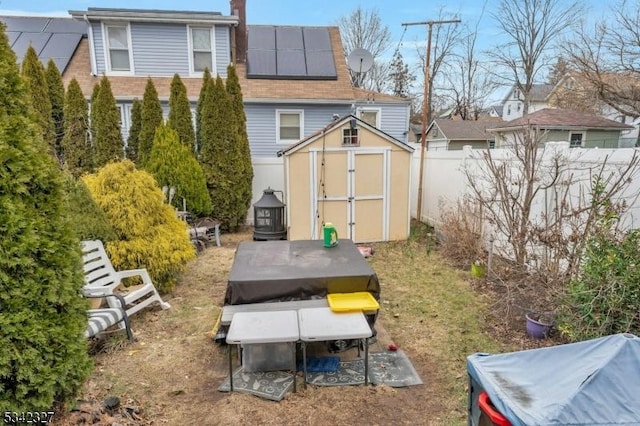 back of house featuring solar panels, a shed, an outdoor structure, and fence