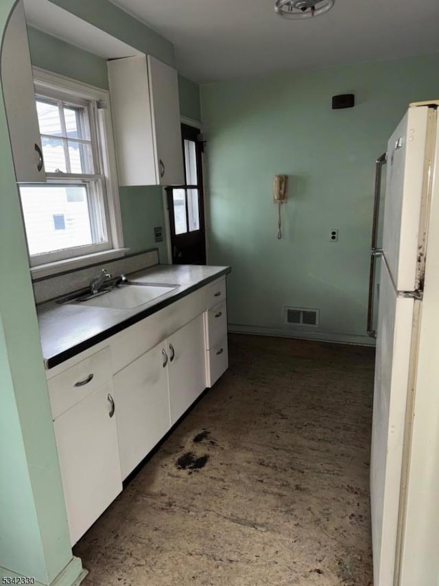 kitchen with a sink, visible vents, white cabinets, and freestanding refrigerator