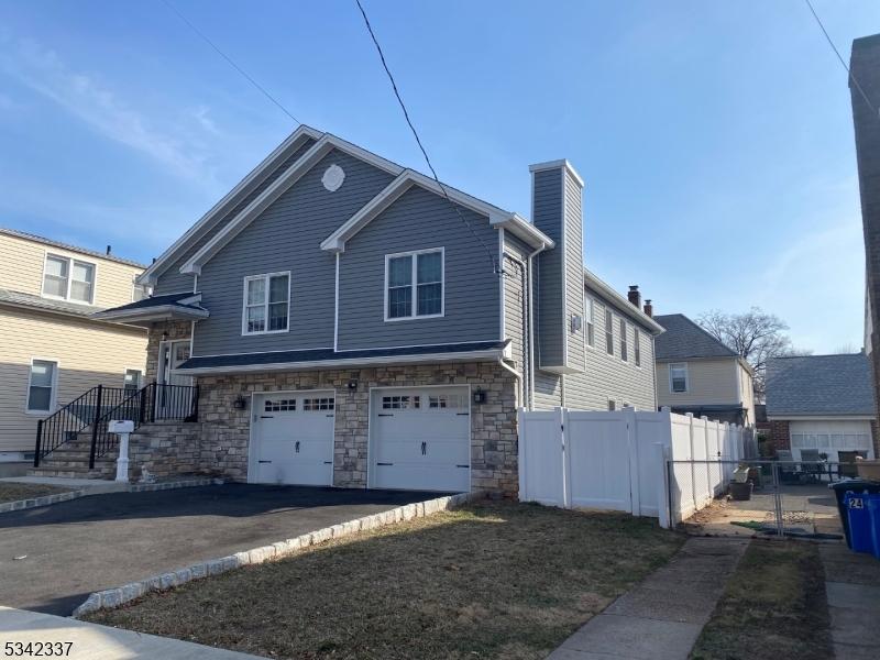 view of front facade with driveway, stone siding, fence, an attached garage, and a chimney