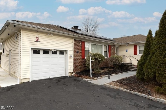 ranch-style home featuring aphalt driveway, roof mounted solar panels, brick siding, and an attached garage