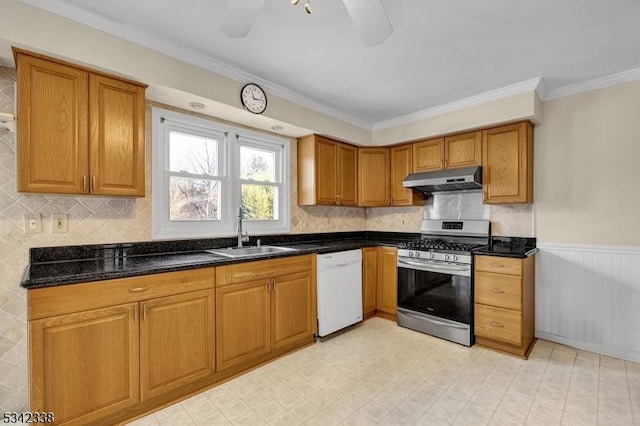 kitchen with white dishwasher, under cabinet range hood, a wainscoted wall, a sink, and gas stove