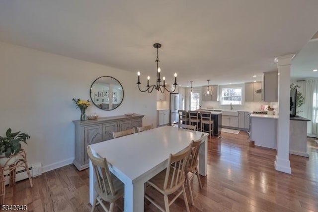 dining room with a notable chandelier, baseboards, baseboard heating, dark wood finished floors, and ornate columns