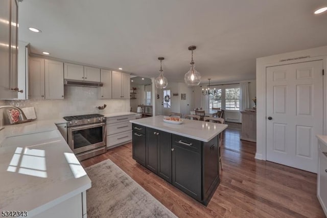 kitchen featuring wood finished floors, high end stainless steel range oven, light countertops, under cabinet range hood, and a sink