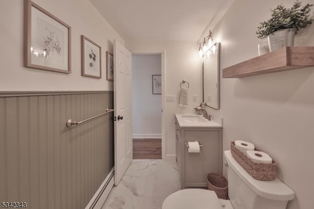 half bath with toilet, a wainscoted wall, vanity, baseboards, and marble finish floor