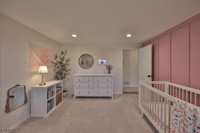 bedroom with recessed lighting, light carpet, a decorative wall, and baseboards