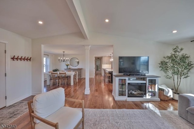 living room featuring decorative columns, recessed lighting, lofted ceiling with beams, an inviting chandelier, and wood finished floors