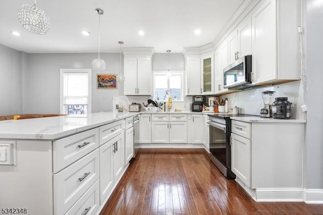 kitchen with light stone countertops, a peninsula, stainless steel appliances, dark wood-style floors, and white cabinetry