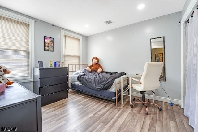 bedroom featuring visible vents, multiple windows, baseboards, and wood finished floors