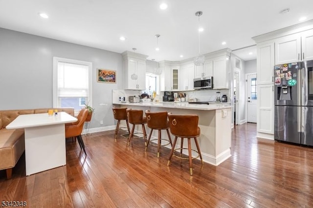 kitchen with a peninsula, appliances with stainless steel finishes, a breakfast bar area, and dark wood finished floors