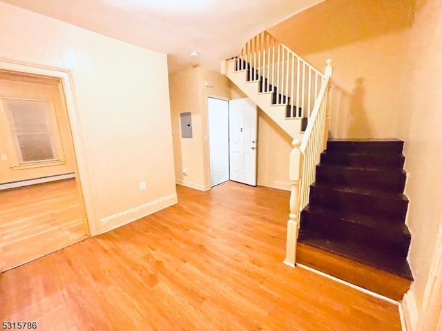 staircase with baseboard heating, wood finished floors, electric panel, and baseboards