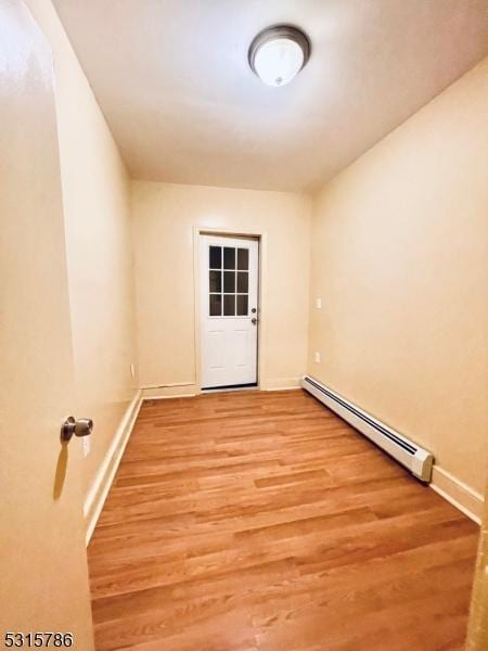 empty room featuring baseboard heating, wood finished floors, and baseboards