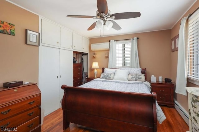 bedroom featuring a baseboard radiator, a closet, a wall mounted AC, a ceiling fan, and wood finished floors