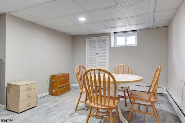 dining area featuring a baseboard heating unit, light wood finished floors, a paneled ceiling, and baseboards