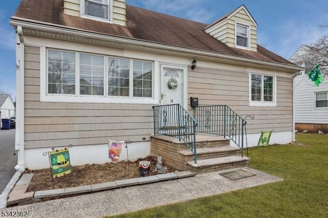 new england style home featuring a shingled roof and a front yard