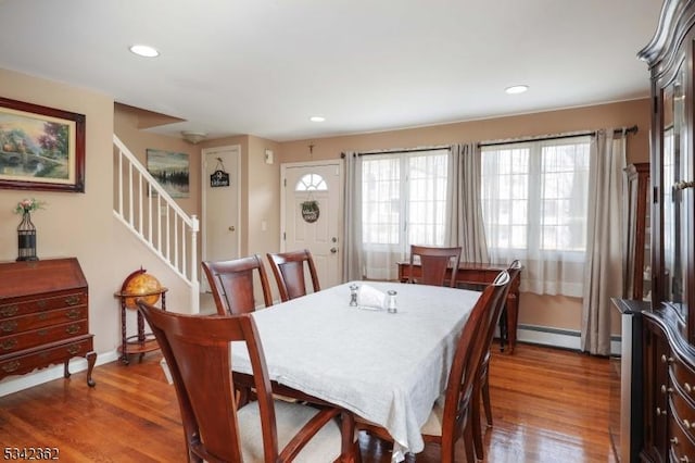 dining space featuring a baseboard heating unit, stairway, wood finished floors, and recessed lighting