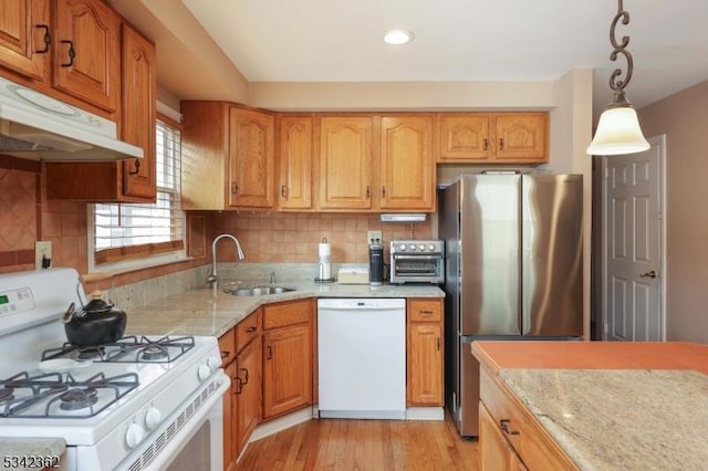 kitchen with light stone countertops, under cabinet range hood, white appliances, a sink, and decorative backsplash