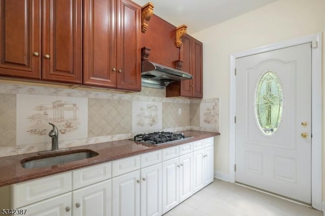 kitchen featuring under cabinet range hood, a sink, dark stone counters, tasteful backsplash, and stainless steel gas stovetop