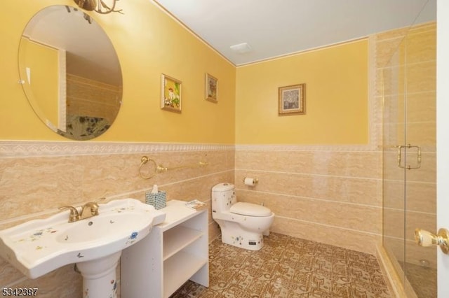 bathroom featuring toilet, a sink, tile walls, wainscoting, and a stall shower