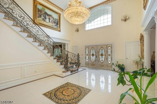 entryway with ornate columns, a high ceiling, a decorative wall, and a notable chandelier