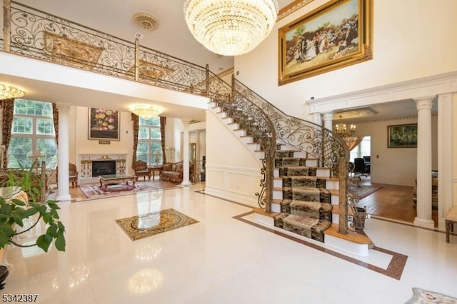 entryway featuring a fireplace, a decorative wall, a high ceiling, an inviting chandelier, and ornate columns