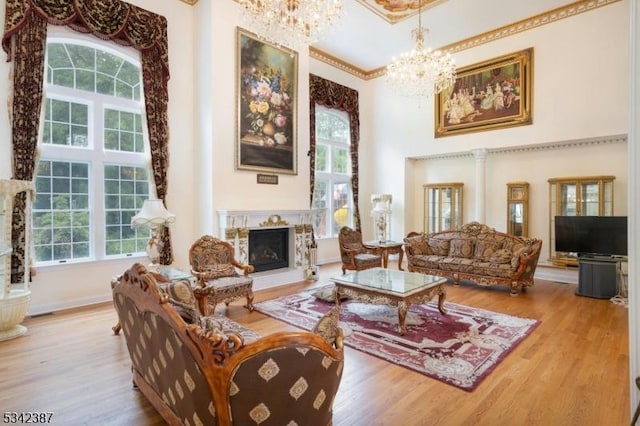 sitting room with a fireplace with raised hearth, a high ceiling, wood finished floors, a wealth of natural light, and an inviting chandelier