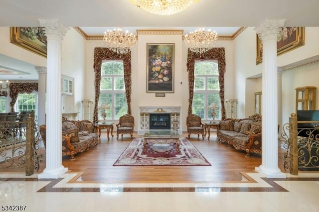 living area featuring an inviting chandelier, a glass covered fireplace, a towering ceiling, and ornate columns