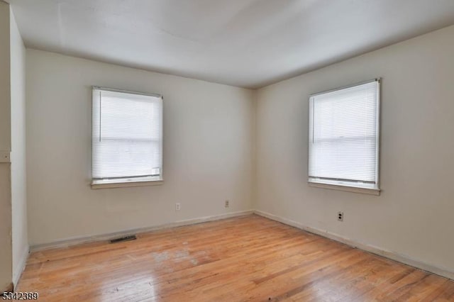 spare room with visible vents, light wood-type flooring, a wealth of natural light, and baseboards