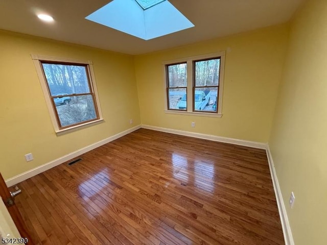 unfurnished room with a skylight, visible vents, baseboards, and wood finished floors