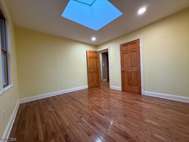 unfurnished bedroom featuring a skylight, baseboards, wood finished floors, and recessed lighting